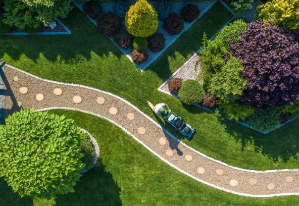 Aerial view of worker mowing lawn as part of scheduled maintenance of garden in a landscaped yard.