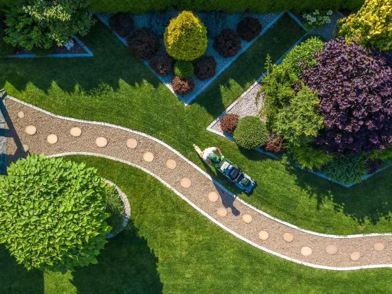 Aerial view of worker mowing lawn as part of scheduled maintenance of garden in a landscaped yard.