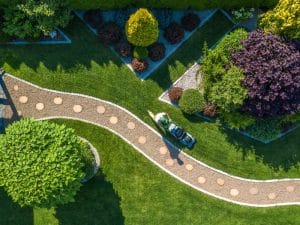 Aerial view of worker mowing lawn as part of scheduled maintenance of garden in a landscaped yard.