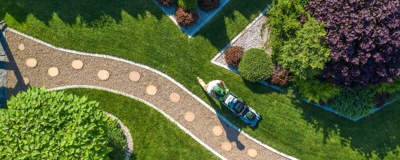 Aerial view of worker mowing lawn as part of scheduled maintenance of garden in a landscaped yard.