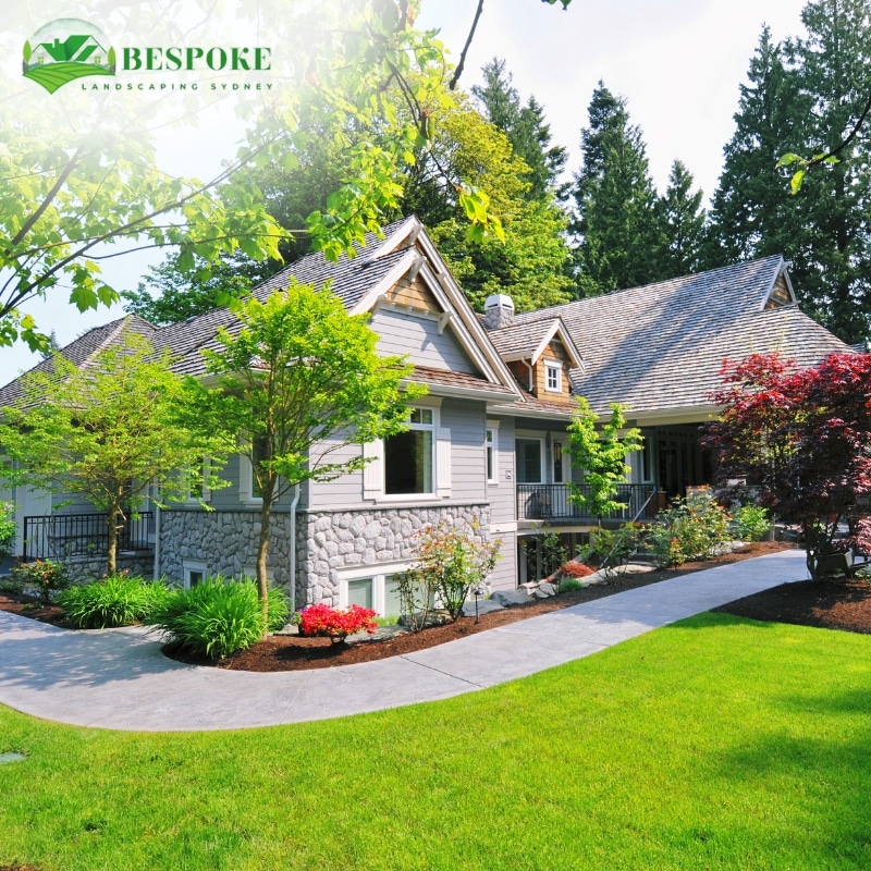 A charming suburban home with stone detailing, surrounded by lush greenery and colorful flowers, showcasing beautiful landscaping in Manly